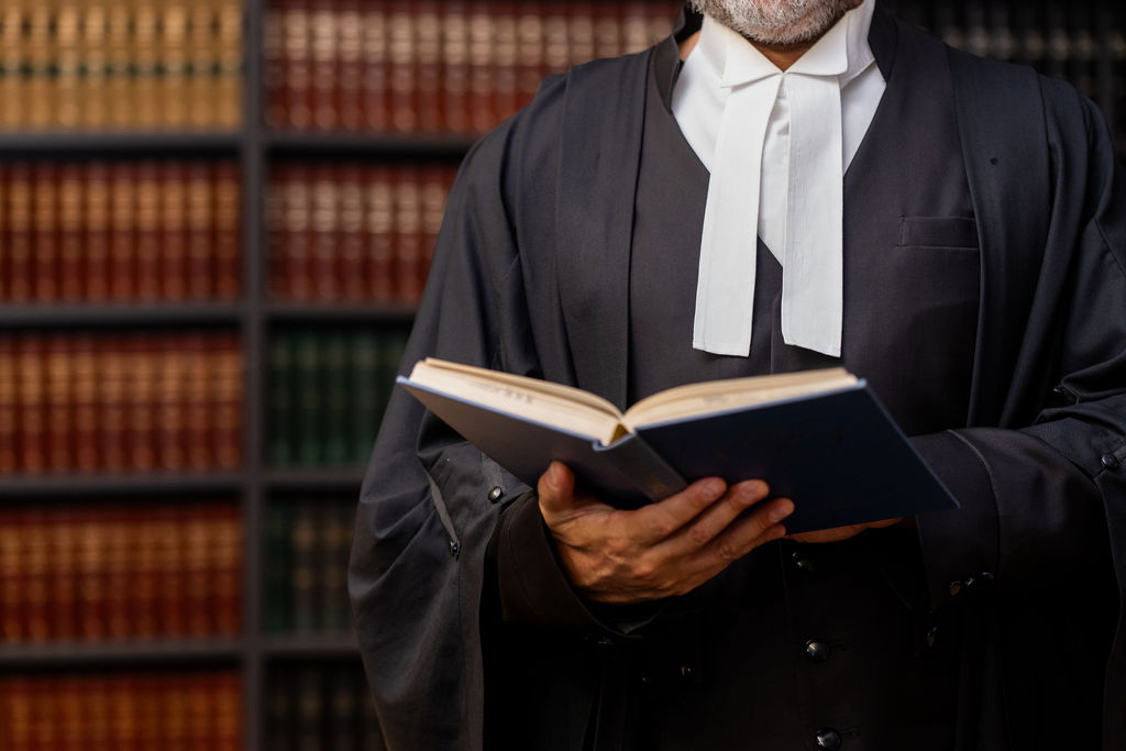 A barrister in robes and bands reading a book in front of a law library
