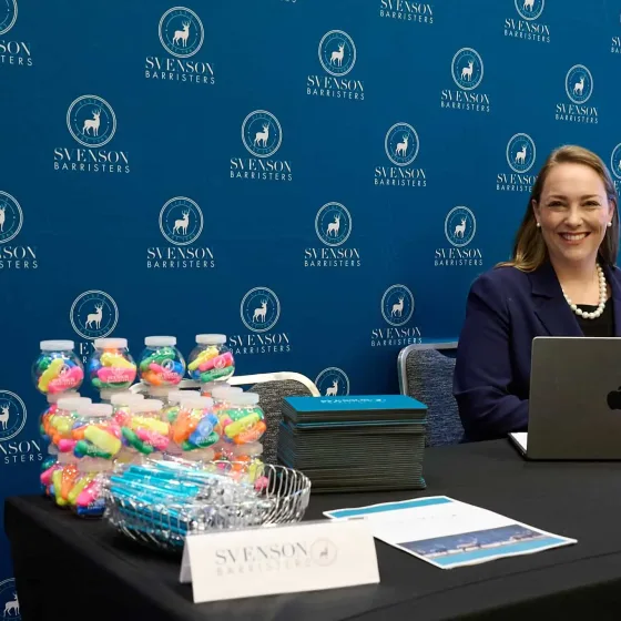 A Svenson Barristers clerk at a desk in front of the branded Svenson Barristers banner